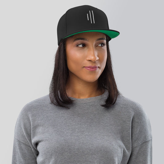 Woman wearing black snapback hat for drummers by Cowbell & Groove, slightly angled front view showing embroidered groove bar logo — minimalist musician gift